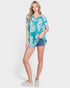 Woman wearing a tropical print shirt and denim shorts on a white background