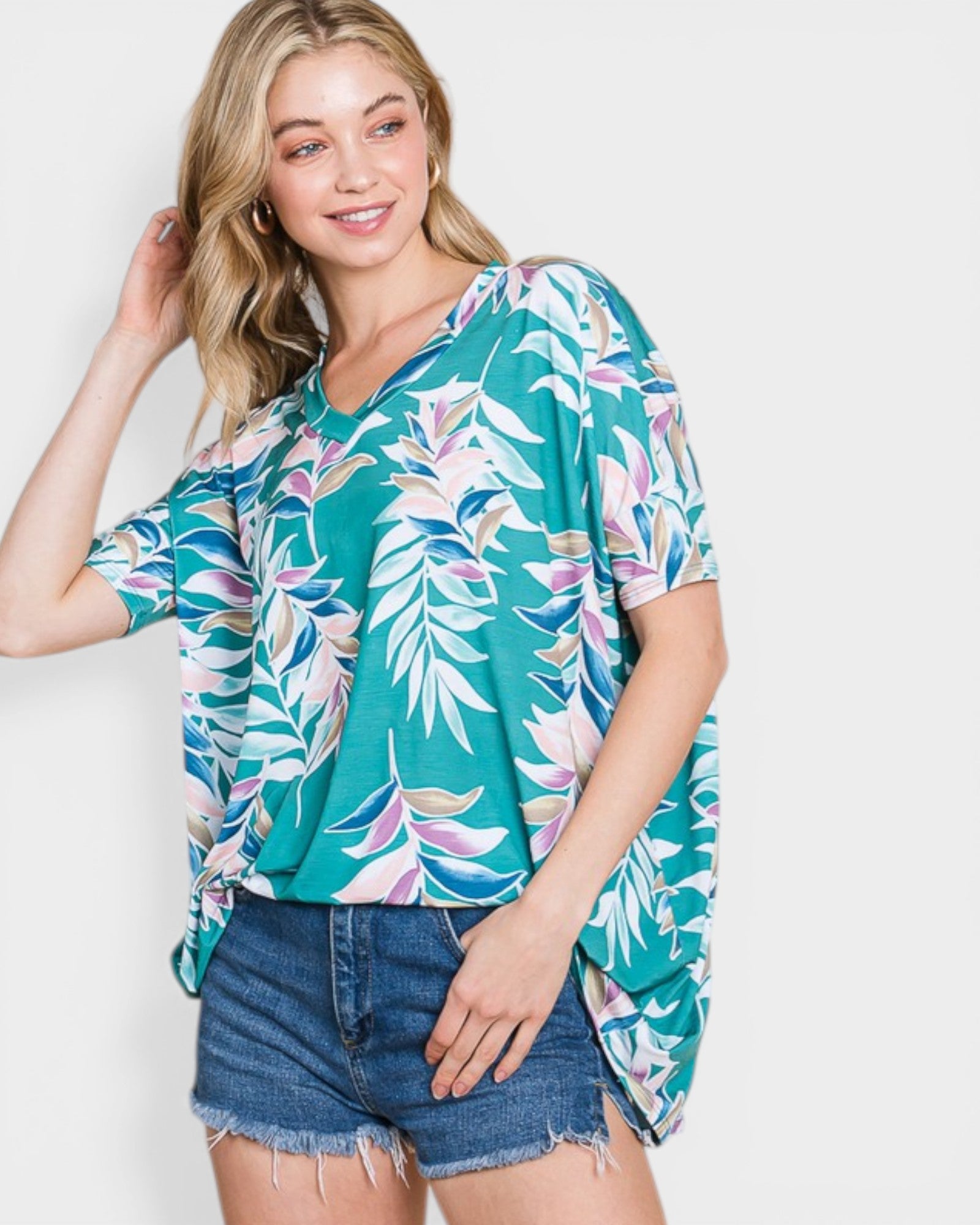 Woman wearing a colorful tropical leaf patterned shirt and denim shorts on a white background