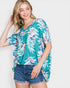 Woman wearing a colorful tropical leaf patterned shirt and denim shorts on a white background