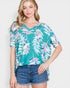 Woman wearing a teal floral blouse and denim shorts on a white background