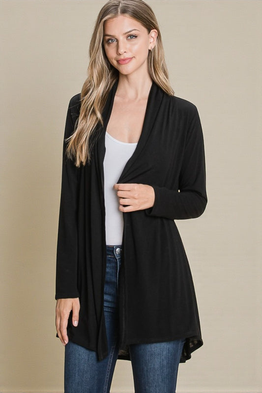 Woman wearing a black cardigan over a white top and blue jeans on a beige background