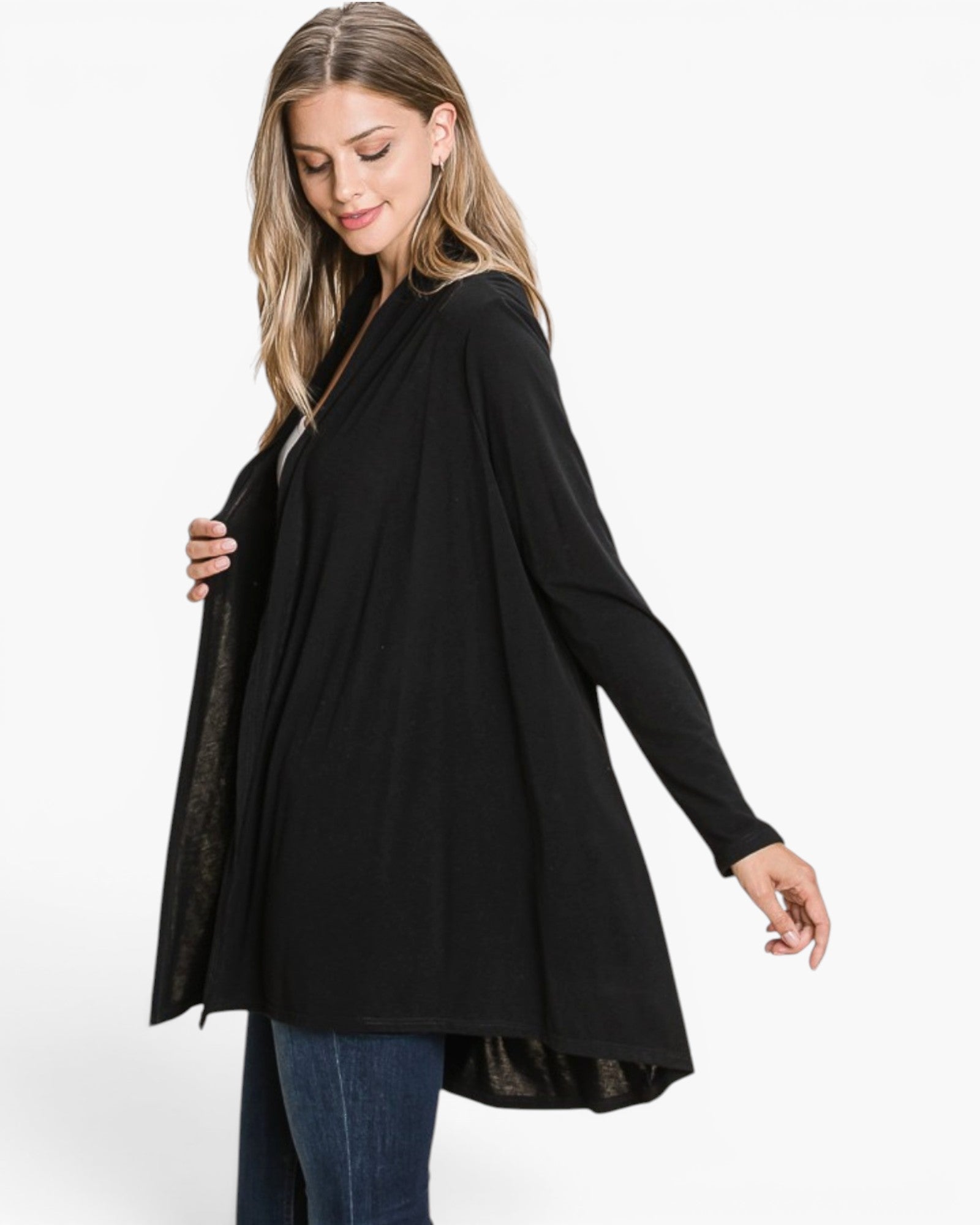A woman modeling a black long-sleeve tunic top with a draped, open-front design, paired with blue jeans against a plain white studio background.