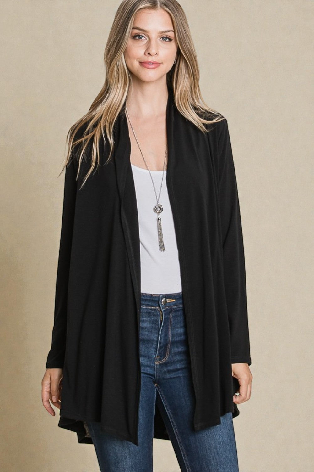 Woman wearing a black cardigan over a white top and blue jeans on a beige background