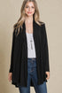 Woman wearing a black cardigan over a white top and blue jeans on a beige background