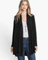A woman modeling a black open-front longline cardigan over a white tank top and blue jeans, photographed against a clean white studio background.