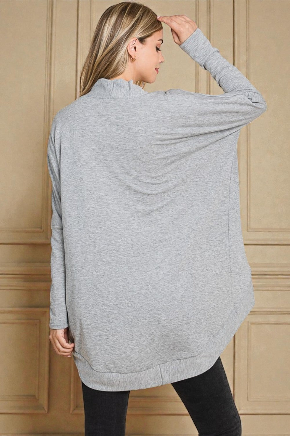 Woman wearing a gray long-sleeve top against a beige paneled wall.