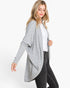A woman modeling a light gray open-front drape cardigan over a white top and dark gray jeans, photographed against a clean white studio background.