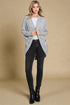 Woman wearing a gray cardigan, white shirt, black jeans, and black boots on a beige background