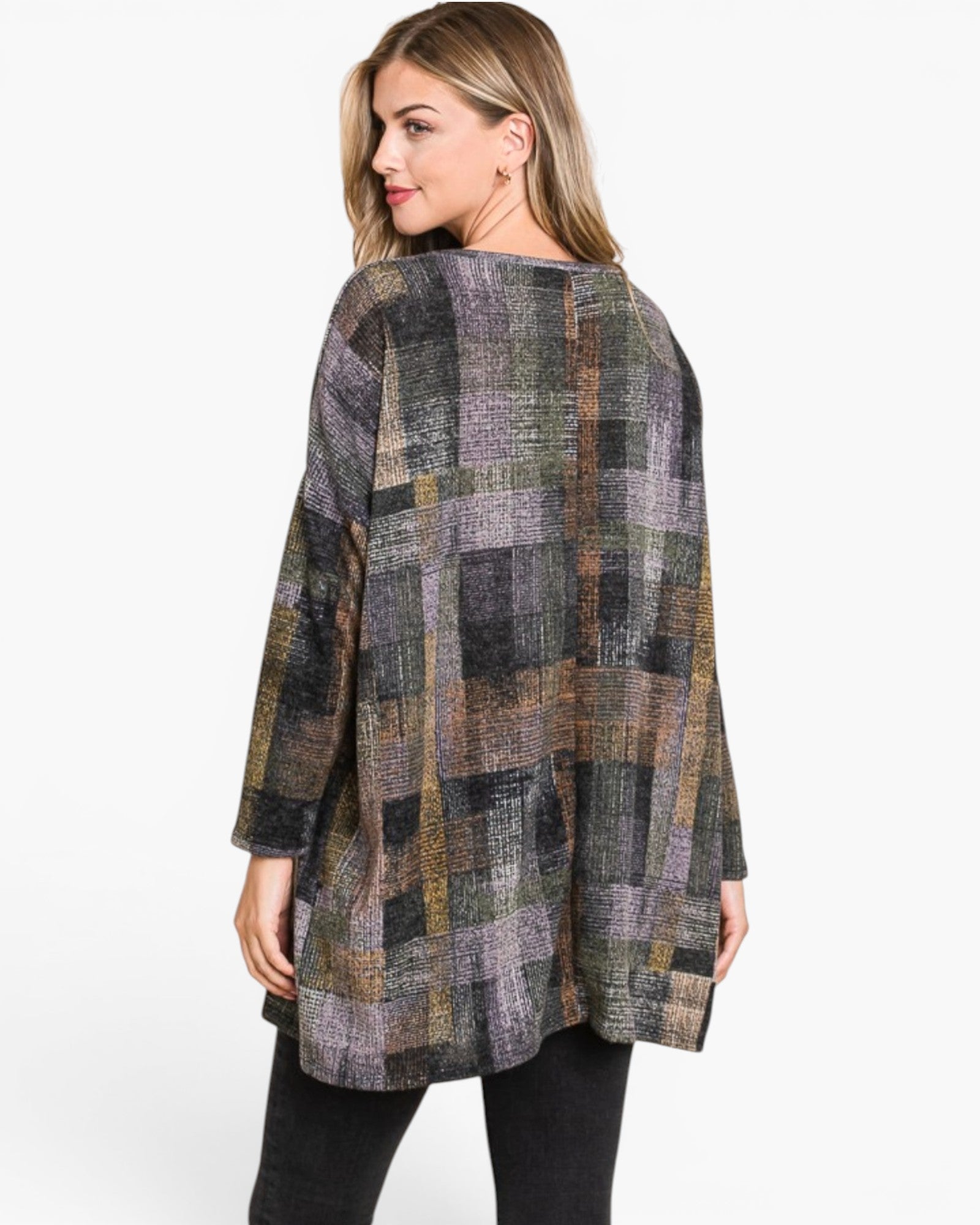 A woman wearing a loose, long-sleeve patchwork plaid tunic top in muted gray, olive green, brown, and purple tones, paired with black pants, shown from a three-quarters back view against a plain white background.
