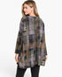 A woman wearing a loose, long-sleeve patchwork plaid tunic top in muted gray, olive green, brown, and purple tones, paired with black pants, shown from a three-quarters back view against a plain white background.