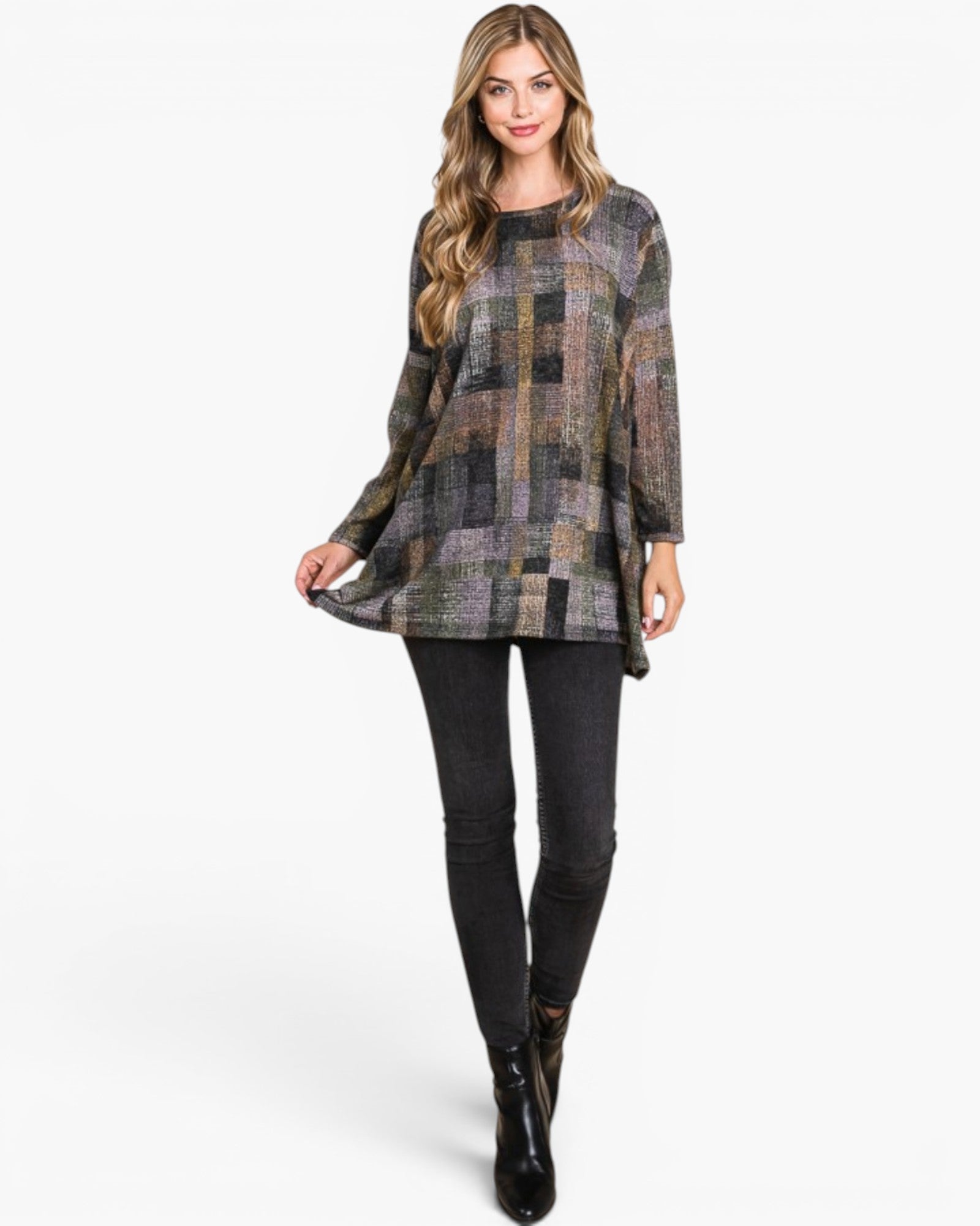 A woman modeling a long-sleeve patchwork tunic top with a multicolor geometric pattern in shades of gray, brown, beige, and black, paired with black skinny pants and black ankle boots, against a plain white studio background.