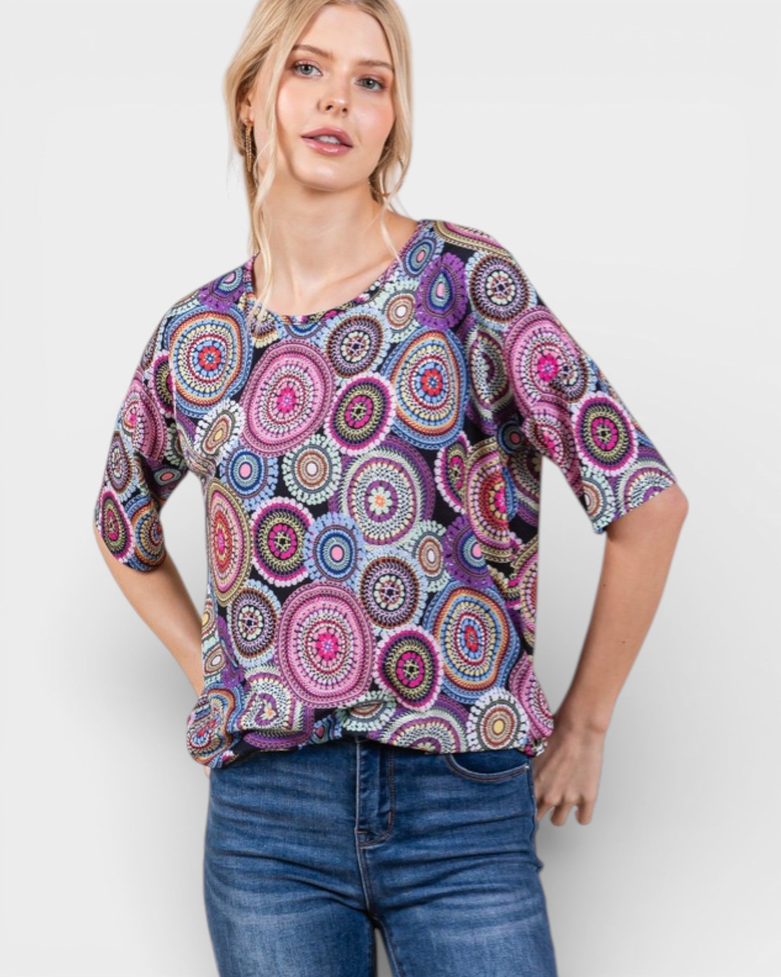 Woman wearing a colorful patterned top and blue jeans on a white background
