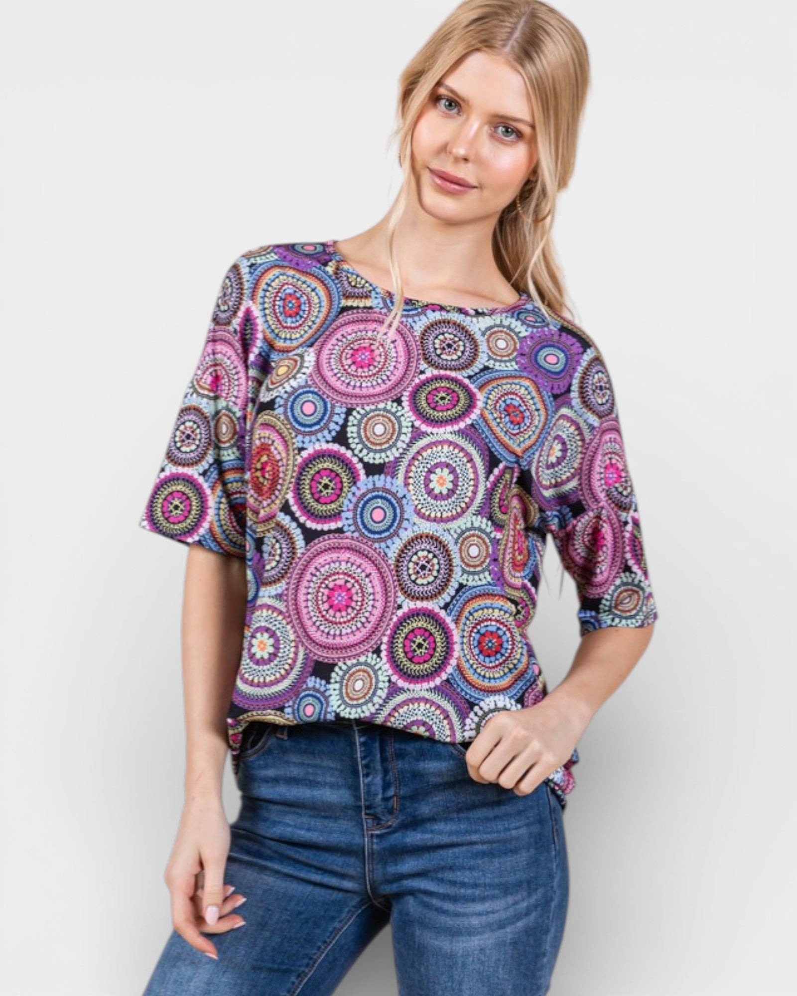 Woman wearing a colorful patterned top and blue jeans on a white background