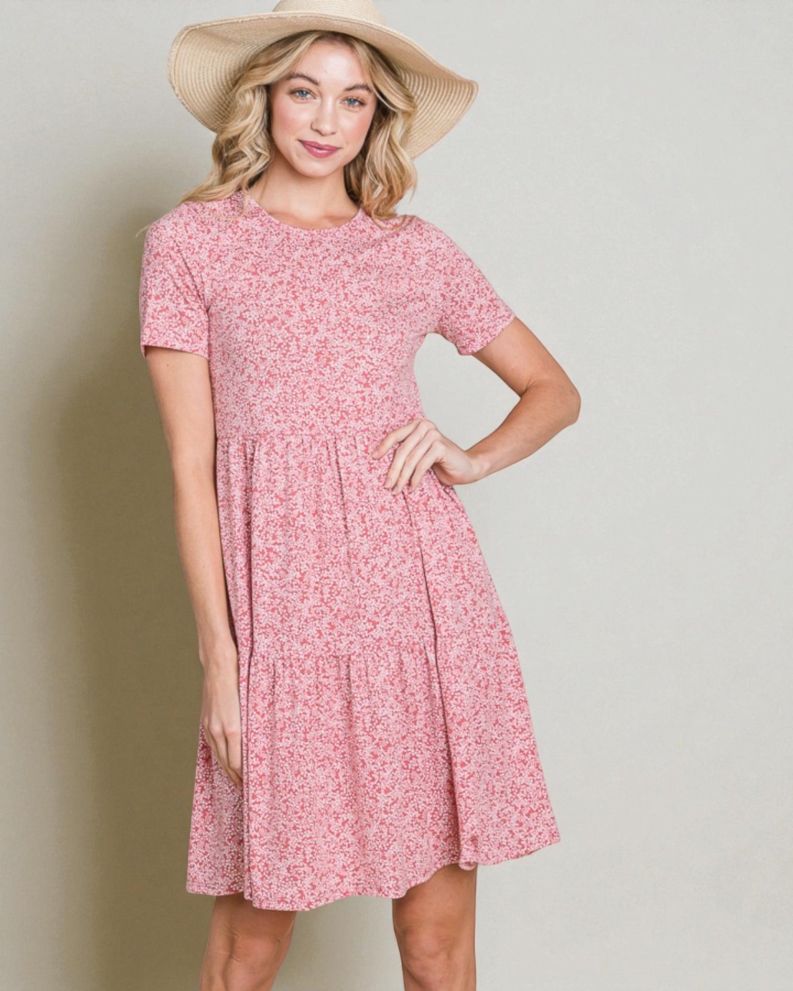 Woman wearing a pink floral dress and straw hat against a plain background