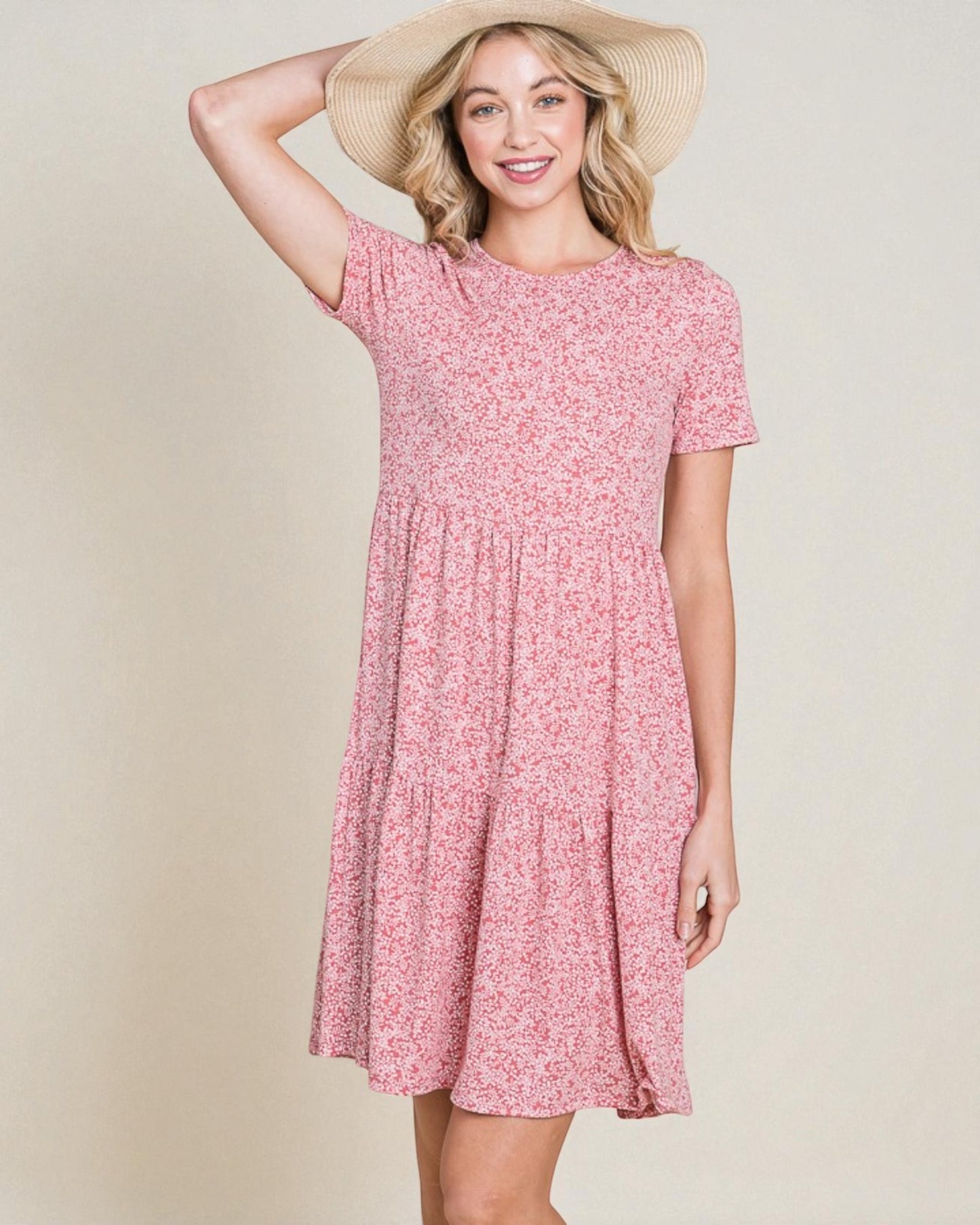 Woman wearing a pink floral dress and straw hat on a beige background