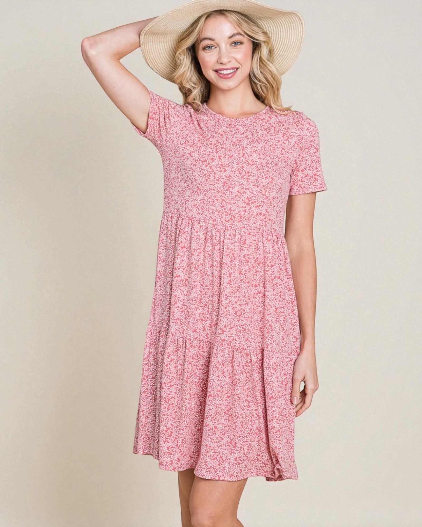 Woman wearing a pink floral dress and straw hat on a beige background