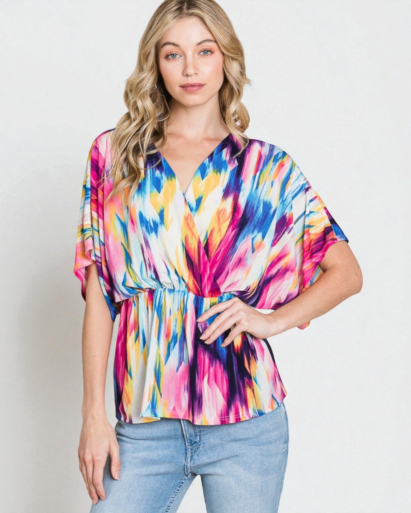 Woman wearing a colorful tie-dye top and jeans on a plain background