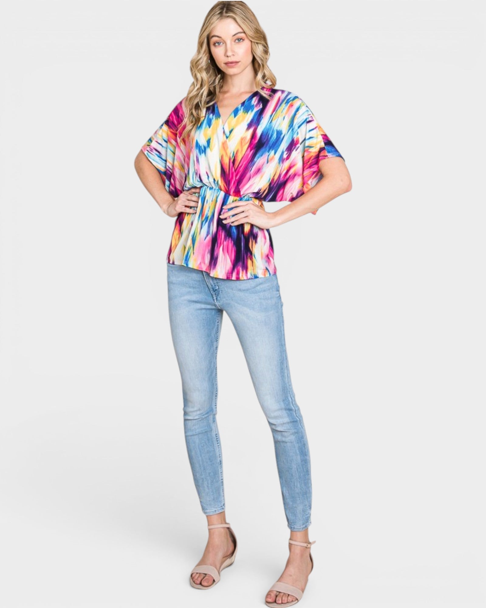 Woman wearing a colorful tie-dye top and light blue jeans on a white background