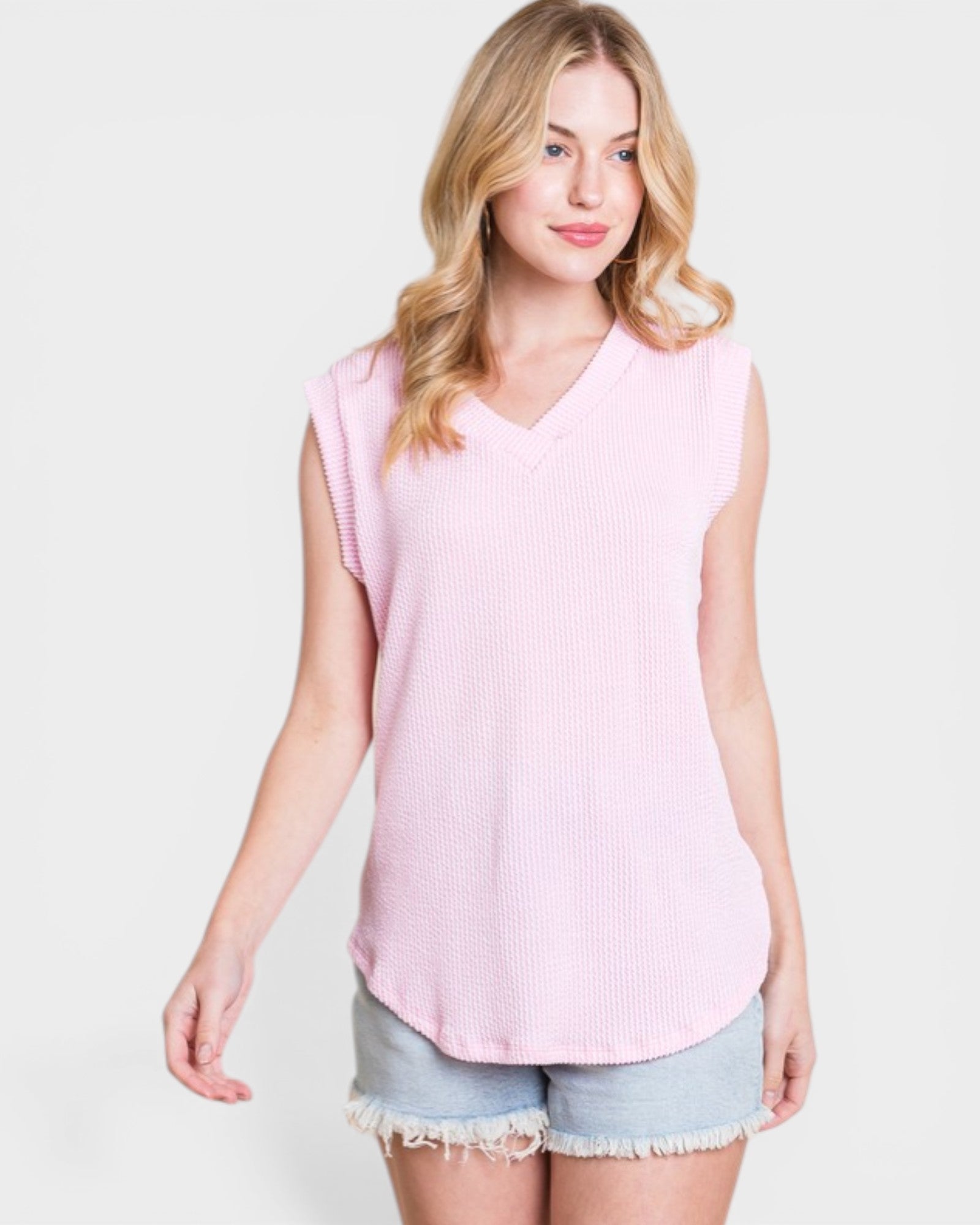 Woman wearing a pink sleeveless top and denim shorts on a white background