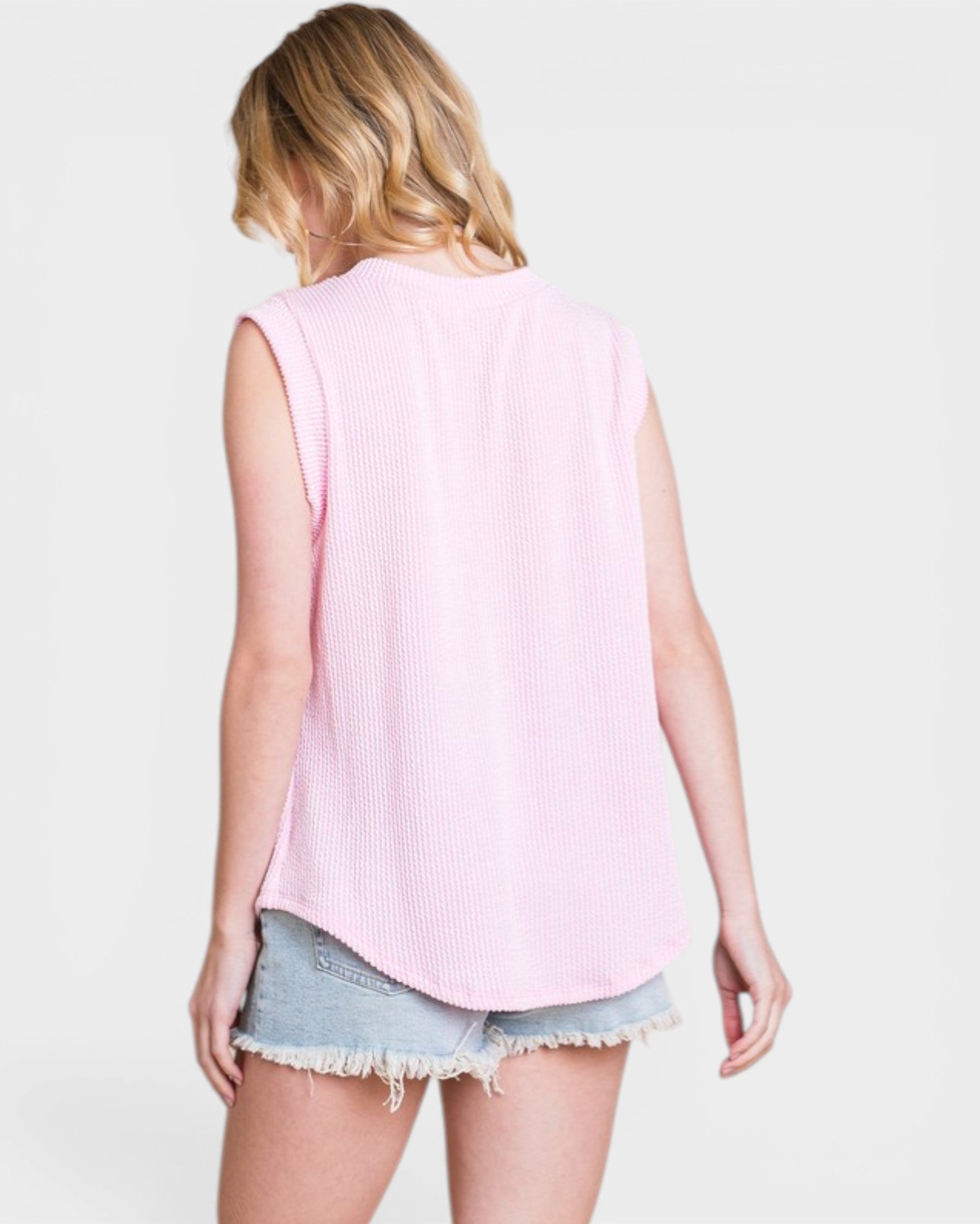 Person wearing a pink sleeveless top and denim shorts on a light background