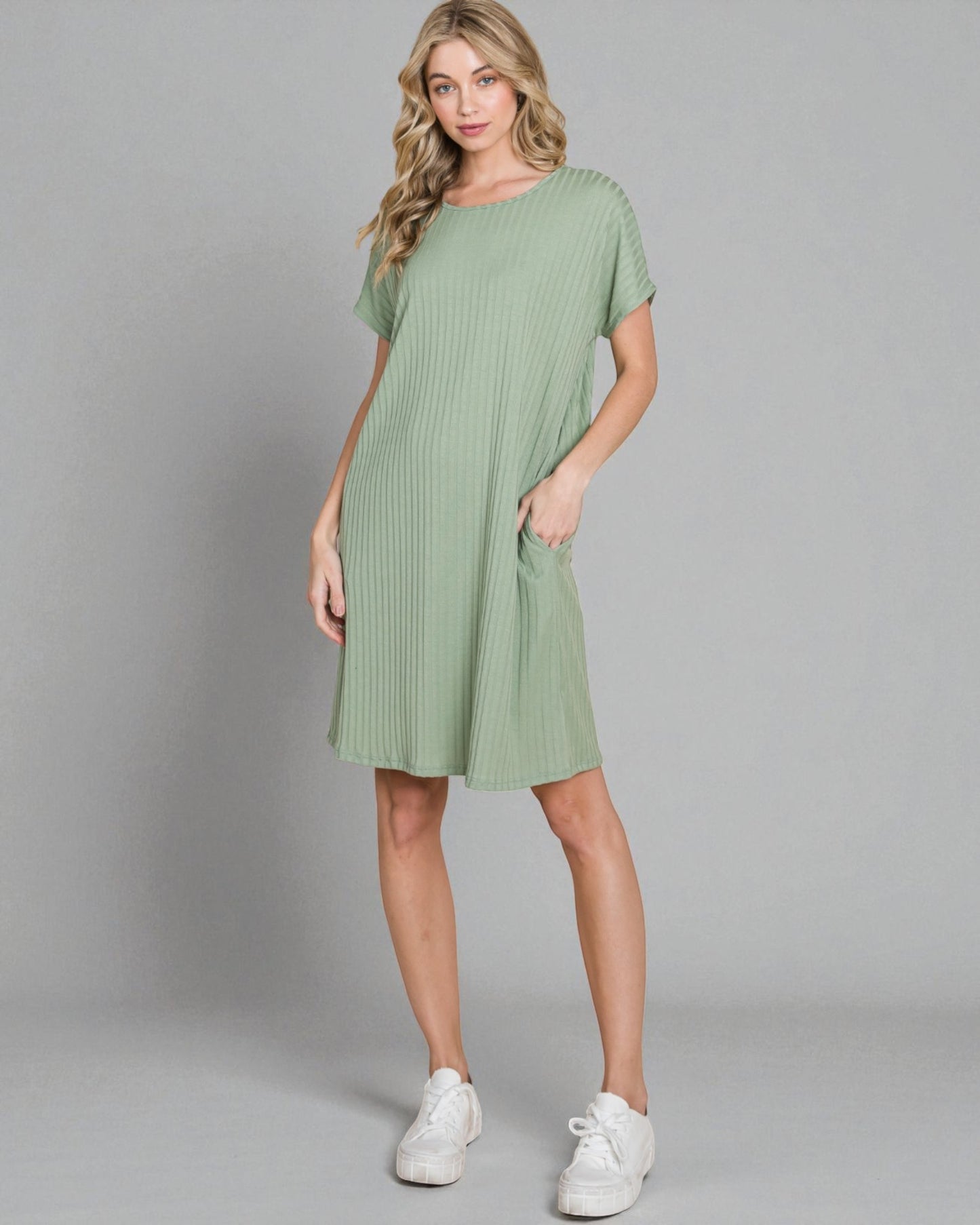 Woman wearing a green dress with white sneakers on a gray background