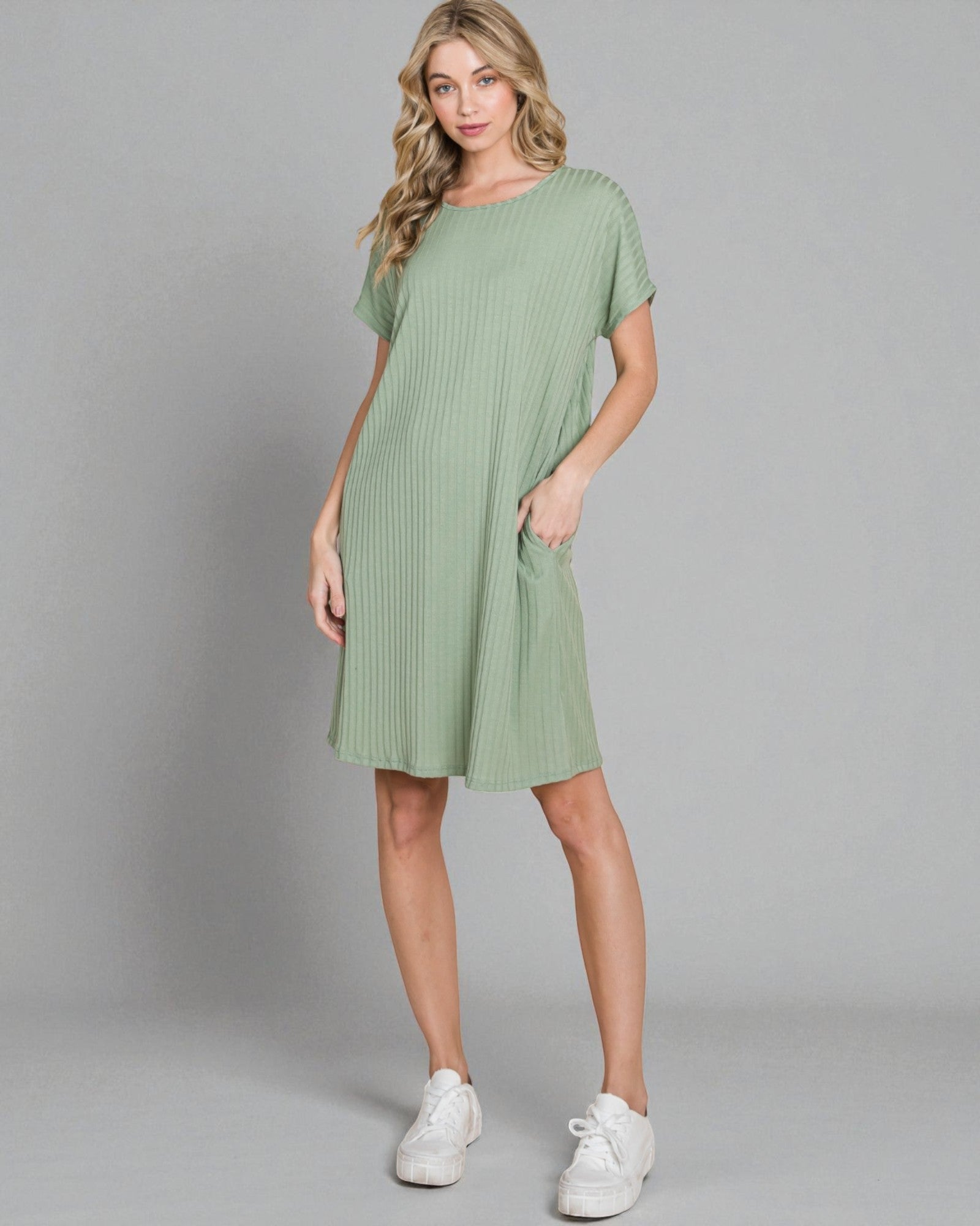 Woman wearing a green dress with white sneakers on a gray background