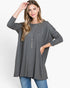 A woman modeling a dark gray long-sleeve tunic top with side pockets, paired with blue jeans and a silver tassel necklace, against a plain white studio background.