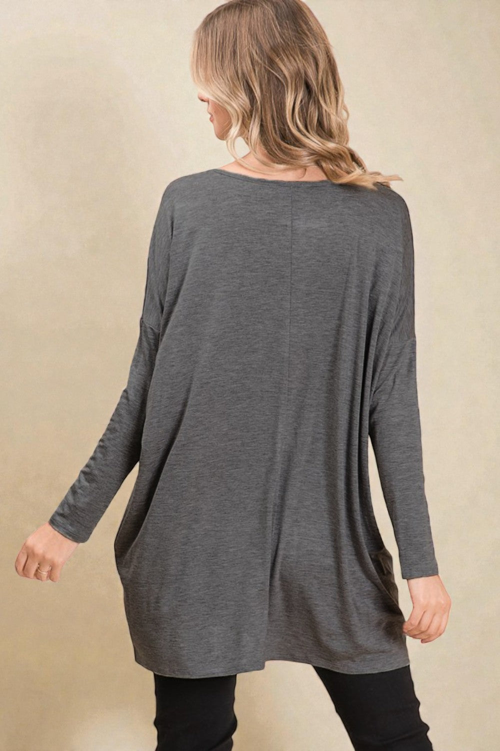 Woman wearing a long-sleeve gray dress against a beige background