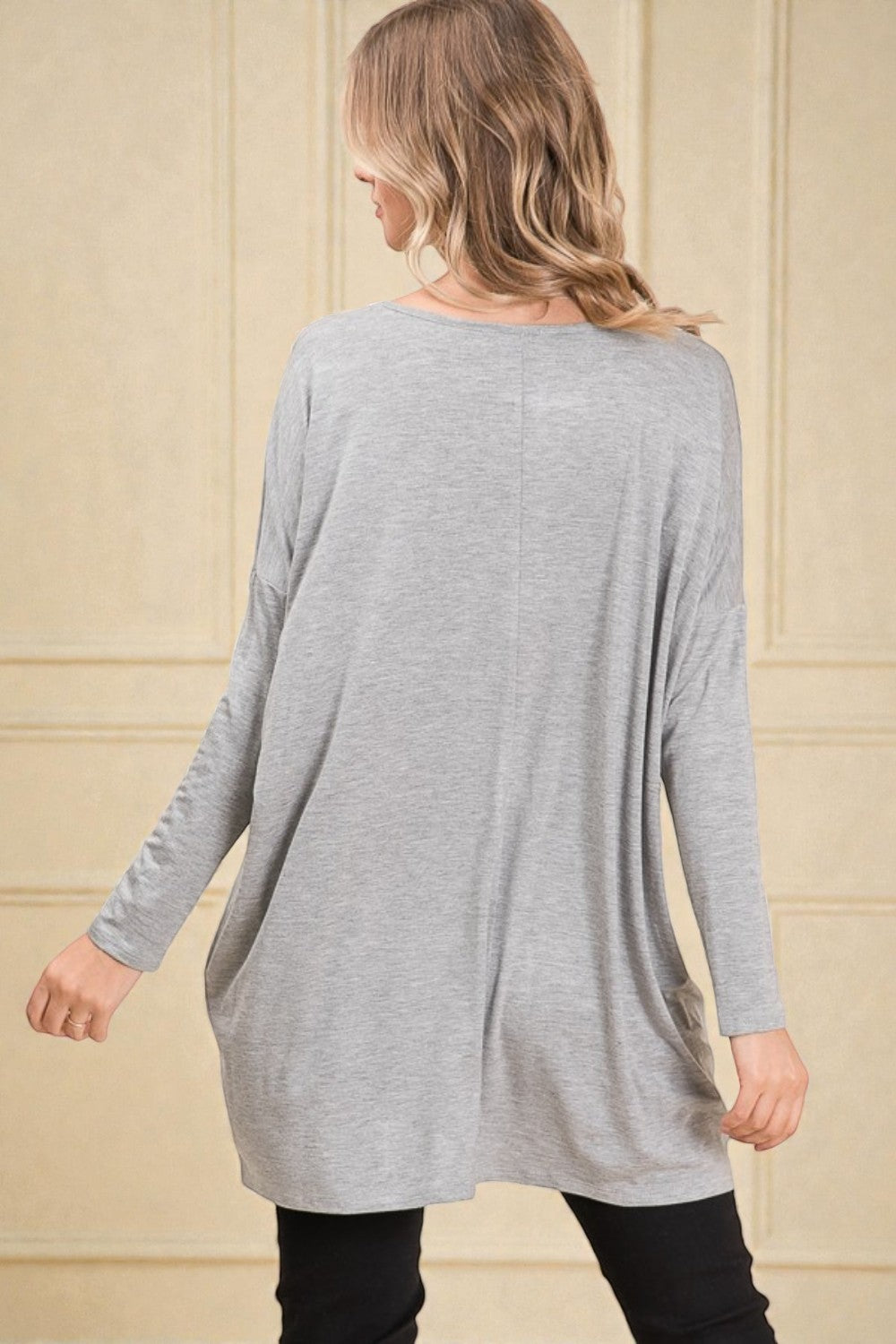 Woman wearing a gray long-sleeve dress against a beige wall.