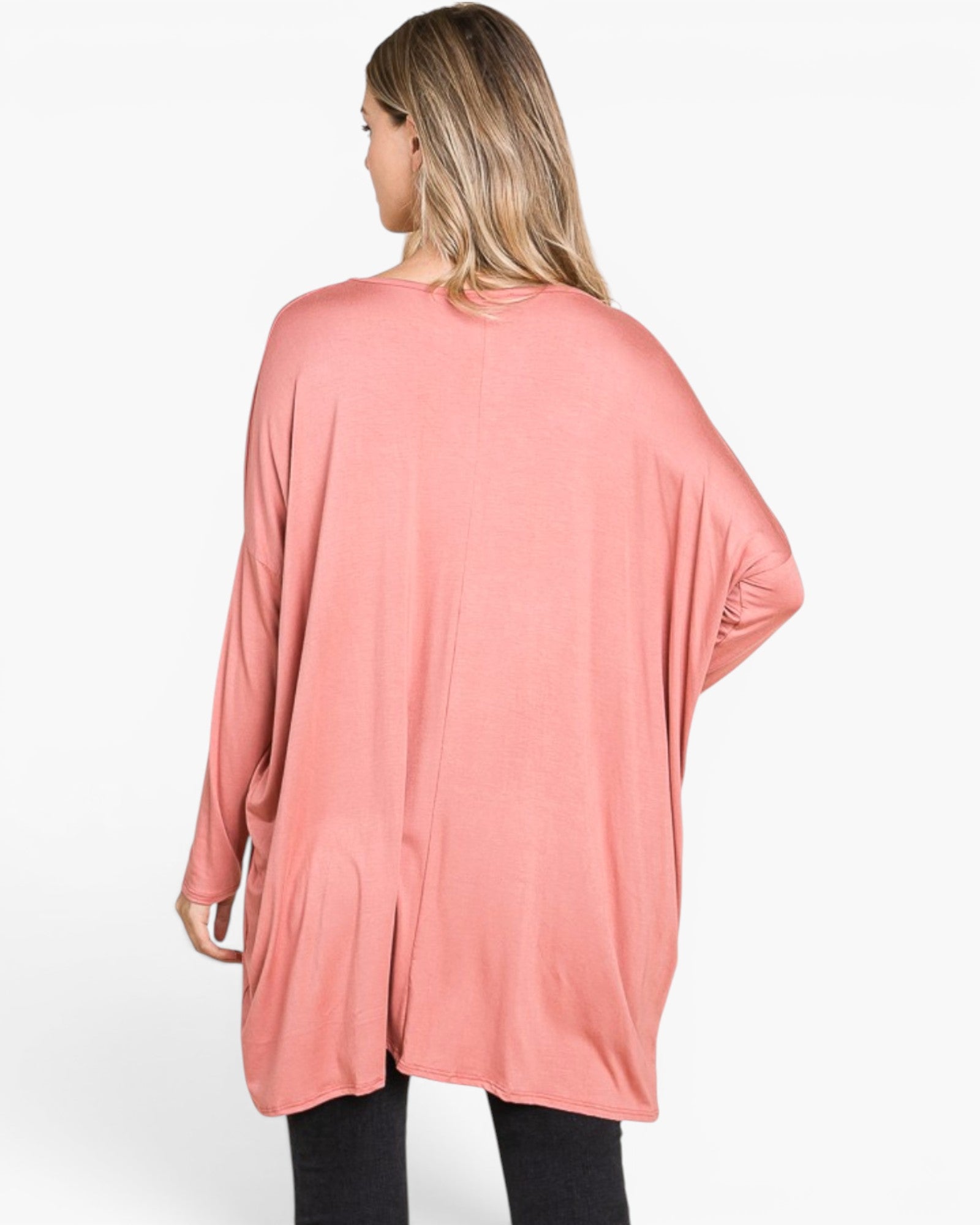 A woman shown from the back wearing a loose, long-sleeve dusty pink tunic top with black pants, photographed against a plain white studio background.