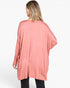 A woman shown from the back wearing a loose, long-sleeve dusty pink tunic top with black pants, photographed against a plain white studio background.