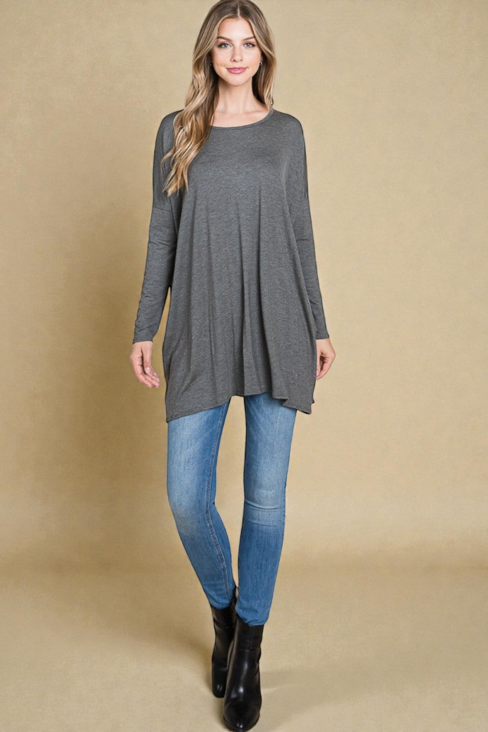 Woman wearing a long gray tunic over blue jeans on a beige background