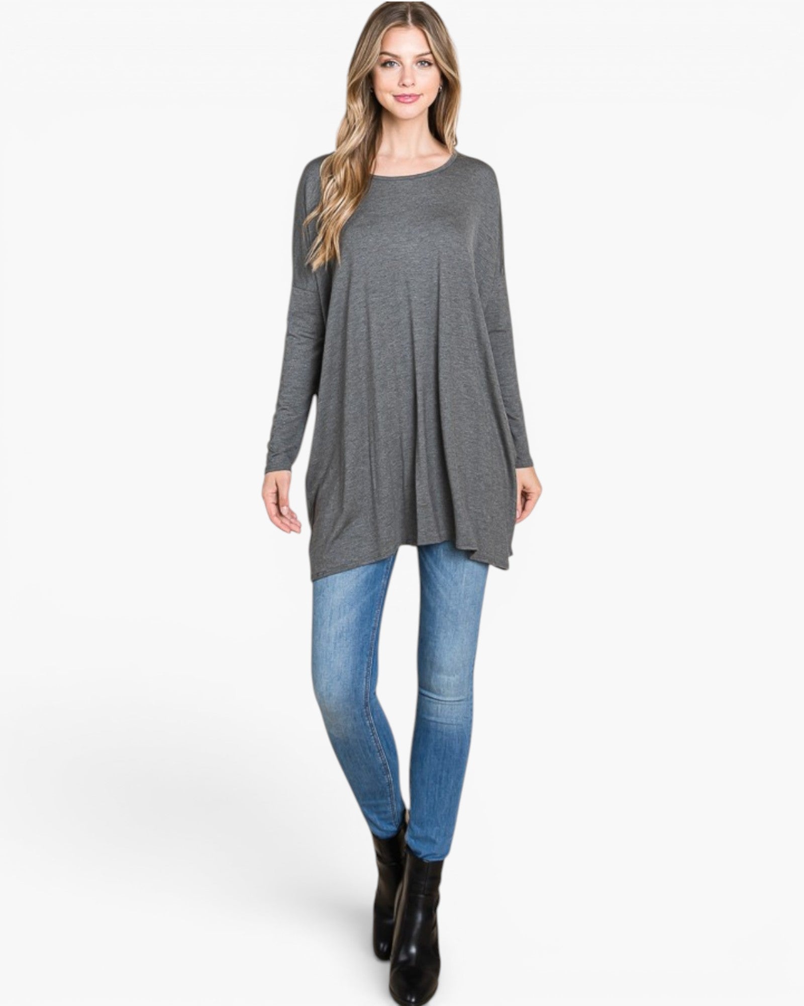 A woman modeling a dark gray long-sleeve tunic top with a relaxed, slightly oversized fit, paired with blue skinny jeans and black ankle boots, against a plain white studio background.