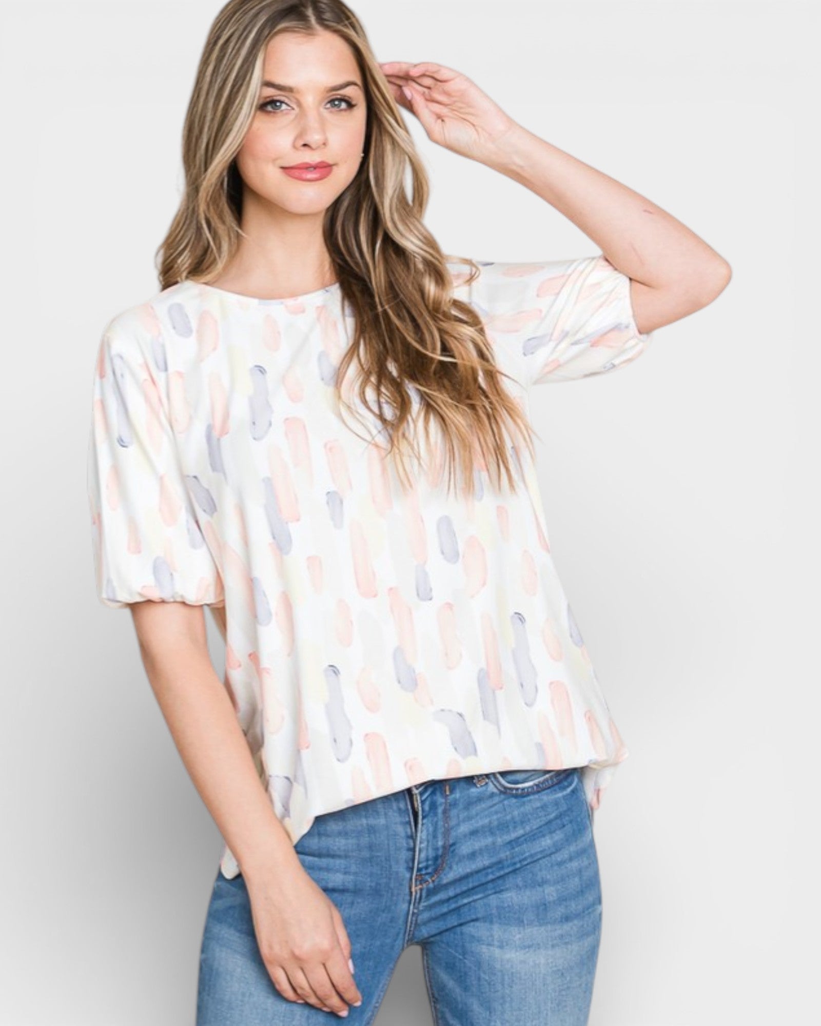 Woman wearing a patterned blouse and jeans on a plain background