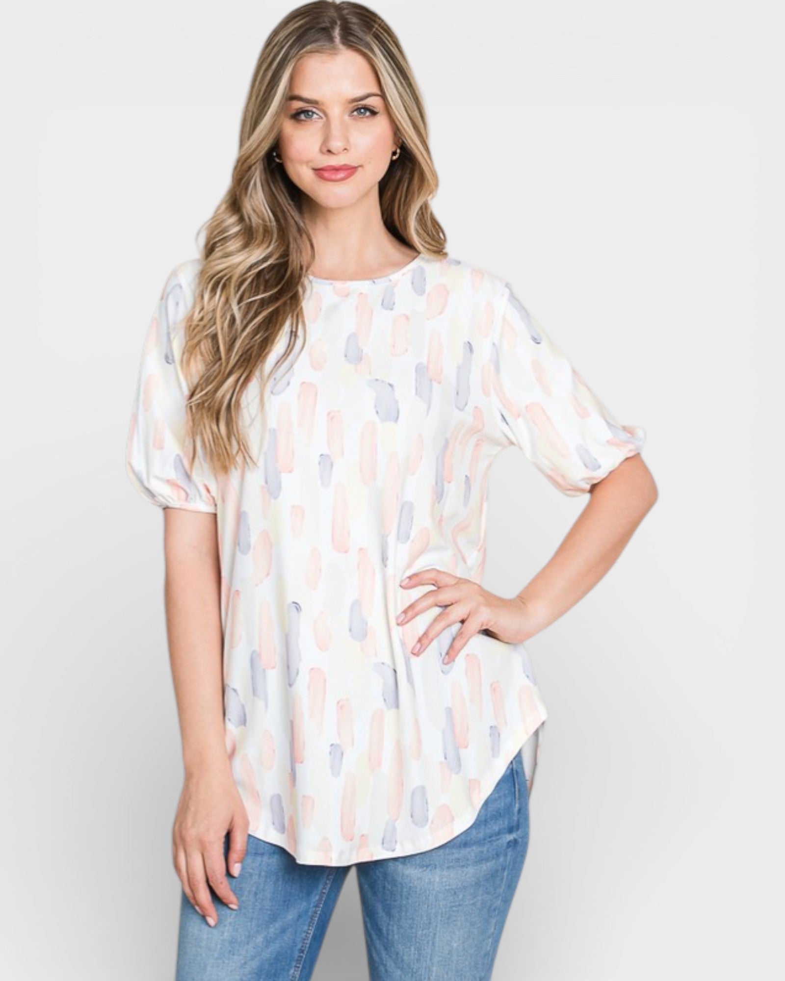 Woman wearing a white blouse with abstract pattern and blue jeans on a plain background