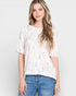 Woman wearing a patterned top and jeans against a plain background