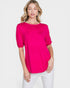 Woman wearing a bright pink top and white pants on a light gray background