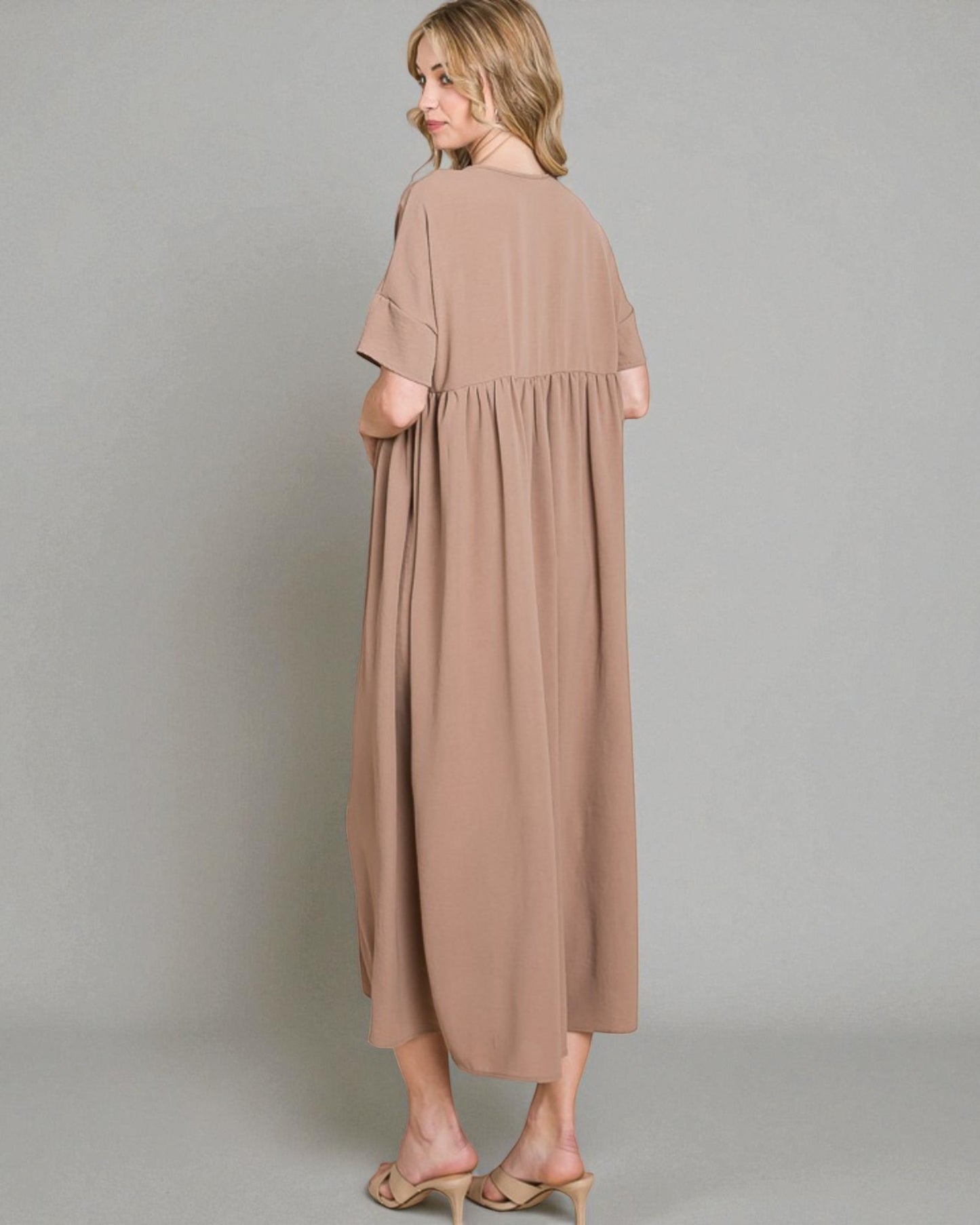 Woman wearing a long beige dress against a plain background