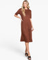 A woman modeling a short-sleeve, knee-length brown dress with a subtle speckled texture, paired with black slide sandals, against a plain white studio background.