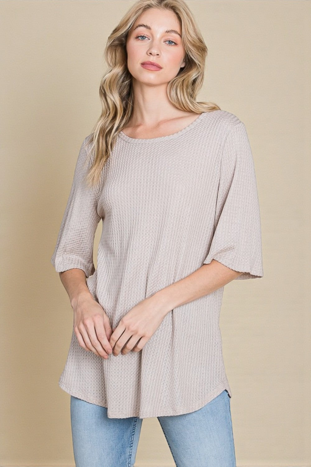 Woman wearing a beige ribbed sweater and light blue jeans against a beige background