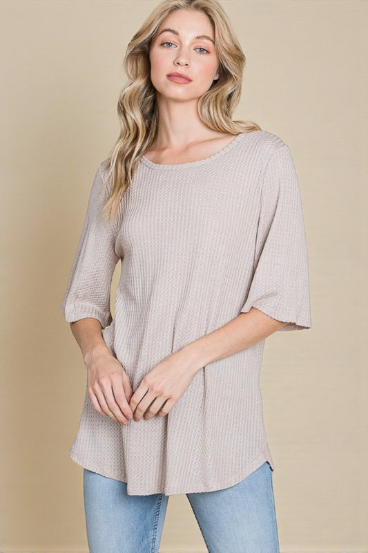 Woman wearing a beige ribbed sweater and light blue jeans against a beige background