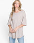 A woman wearing a light beige ribbed knit top with three-quarter sleeves and a relaxed fit, paired with blue jeans, against a plain white studio background.