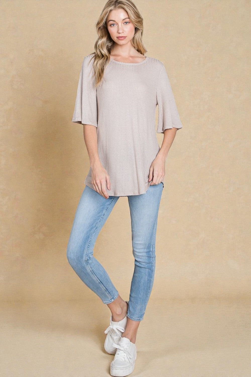 Woman wearing a light gray top and blue jeans against a beige background