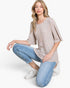 A woman crouching in a studio setting, wearing a light beige waffle-knit short-sleeve top, light blue cropped jeans, and white sneakers.
