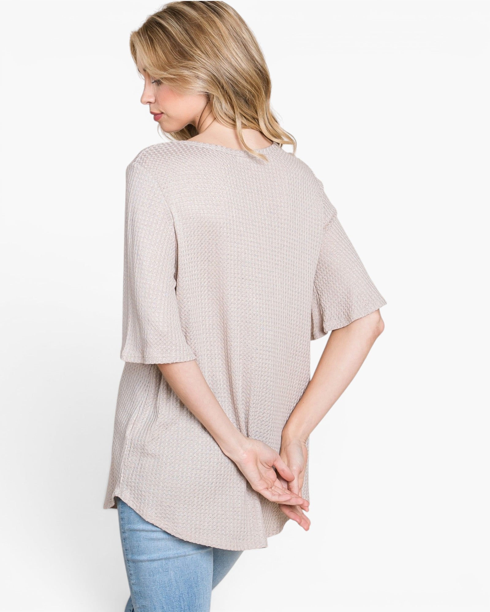 A woman wearing a light beige waffle-knit short-sleeve top, shown from a back-three-quarter view against a plain white background.