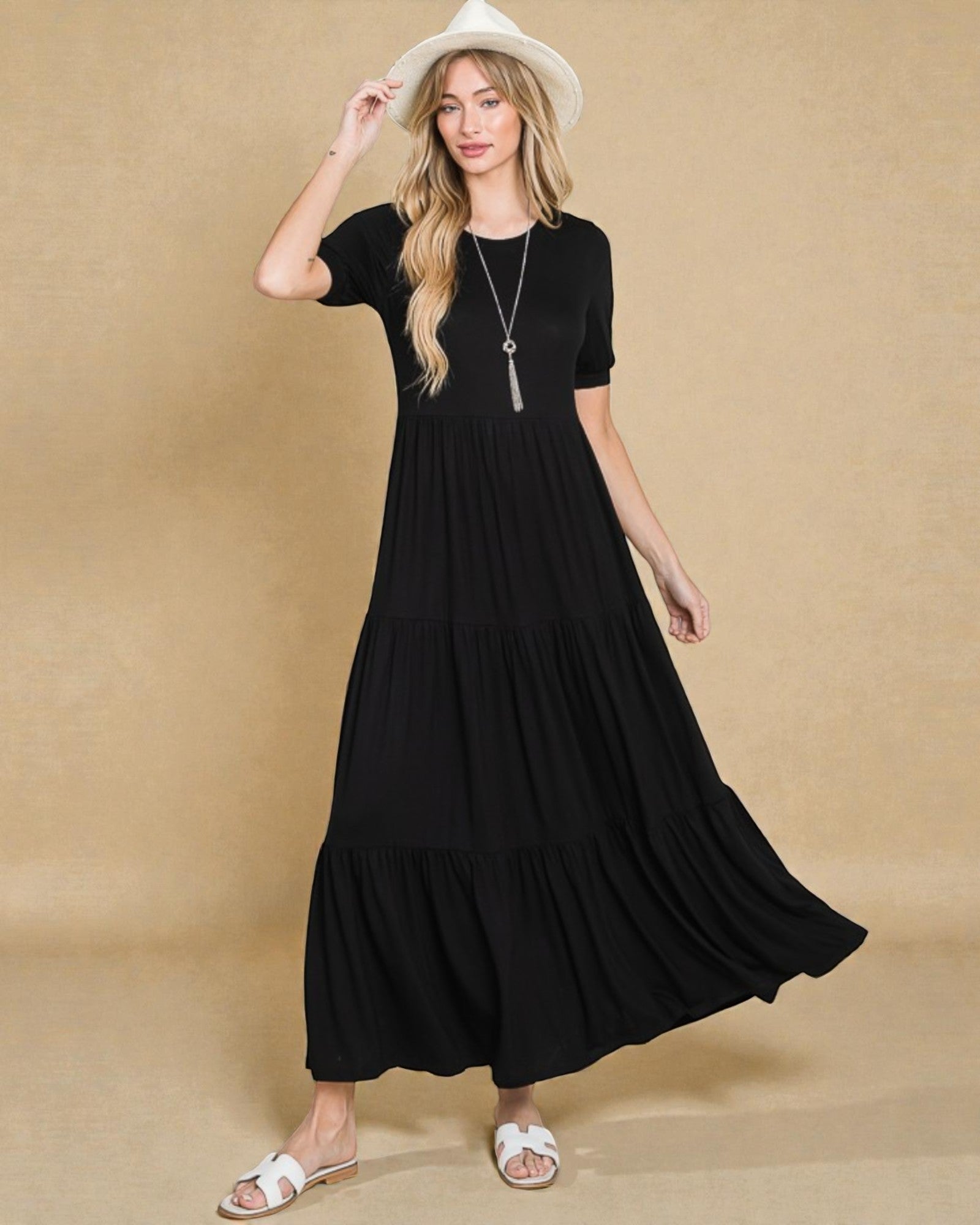 Woman wearing a black dress and white sandals against a beige background