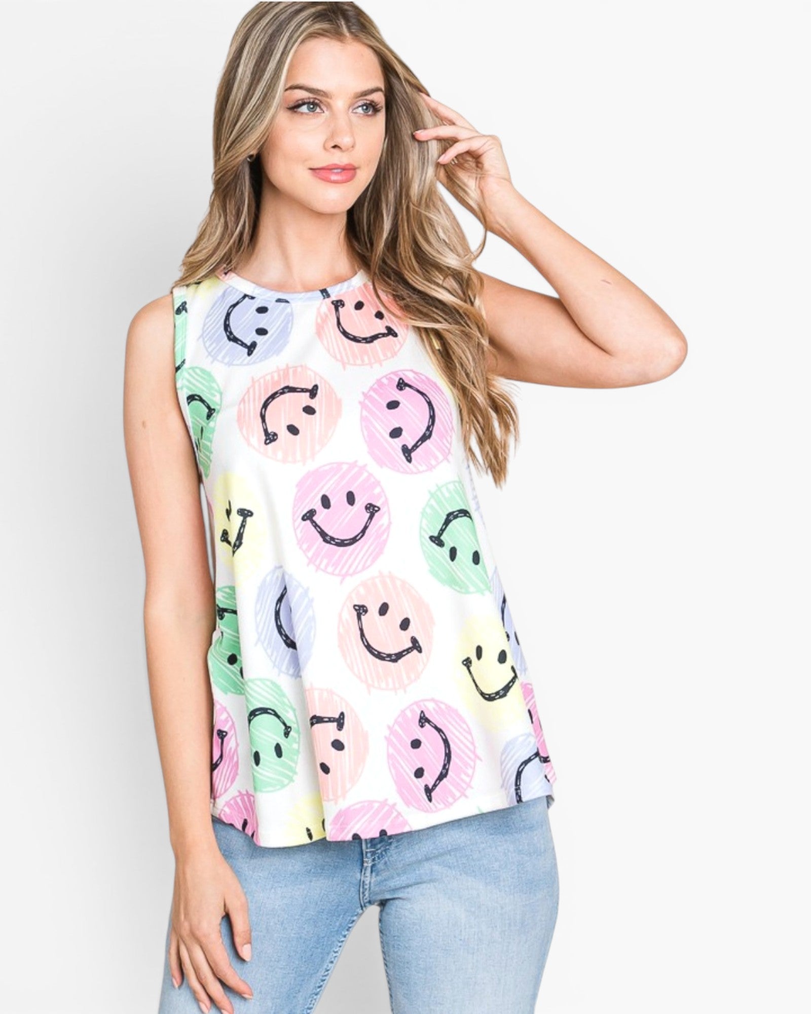 A woman modeling a sleeveless white top with a colorful smiley face pattern, paired with light blue jeans, against a plain white background.