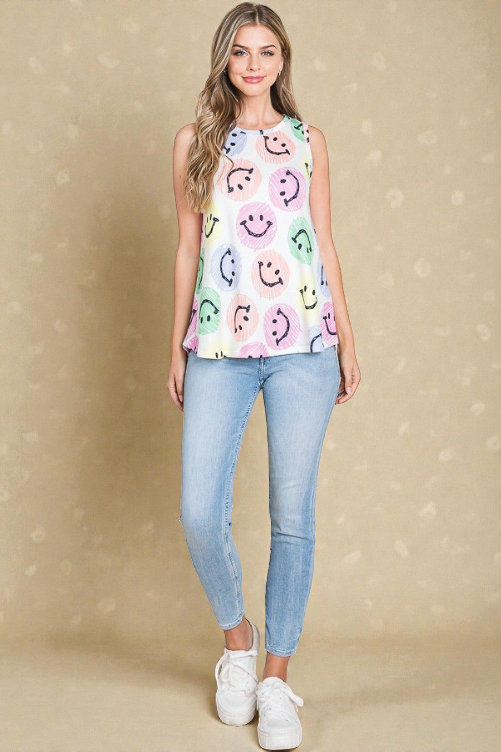 Woman wearing a colorful smiley face top and light blue jeans on a beige background