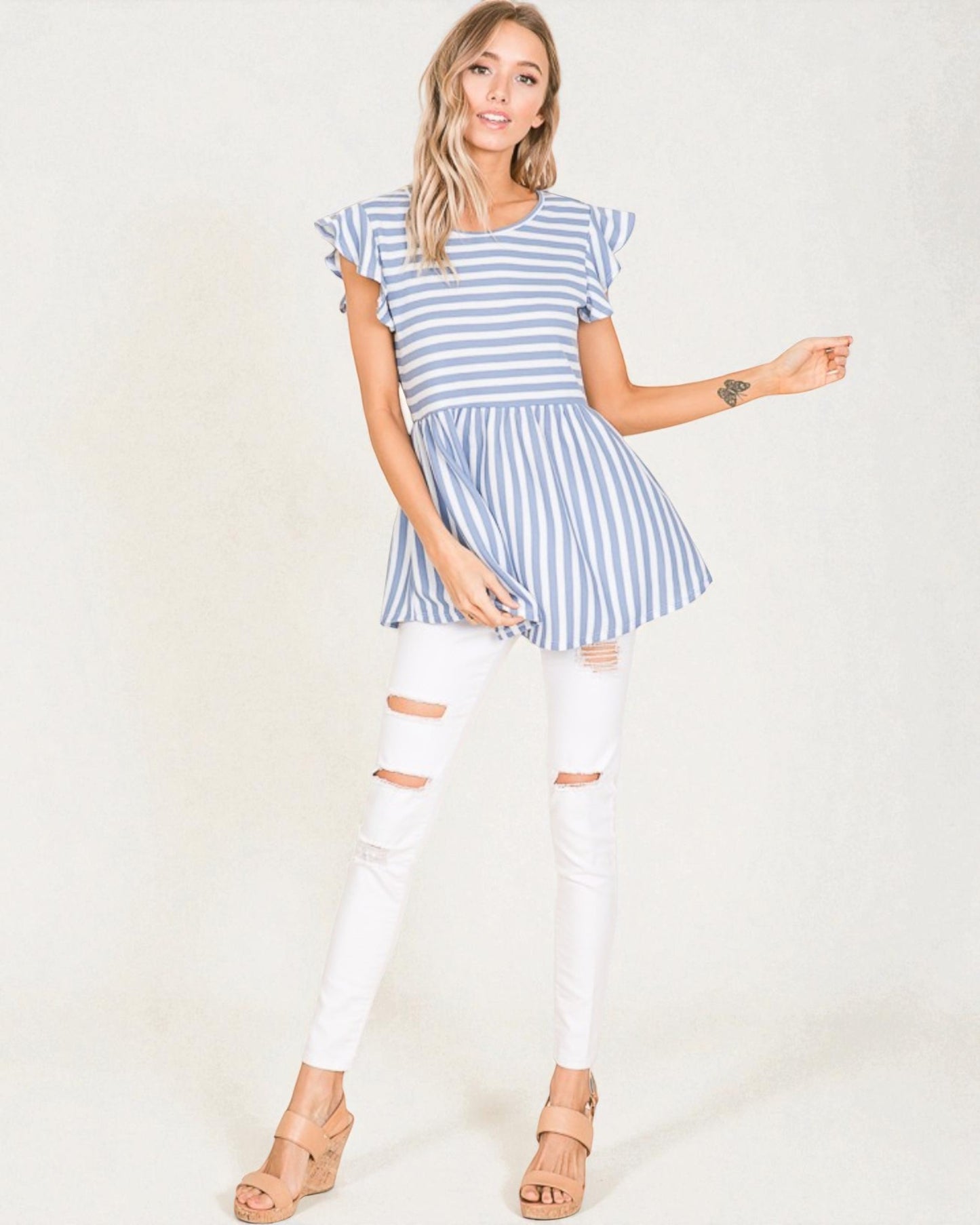 Woman wearing a blue and white striped dress with white pants on a plain background