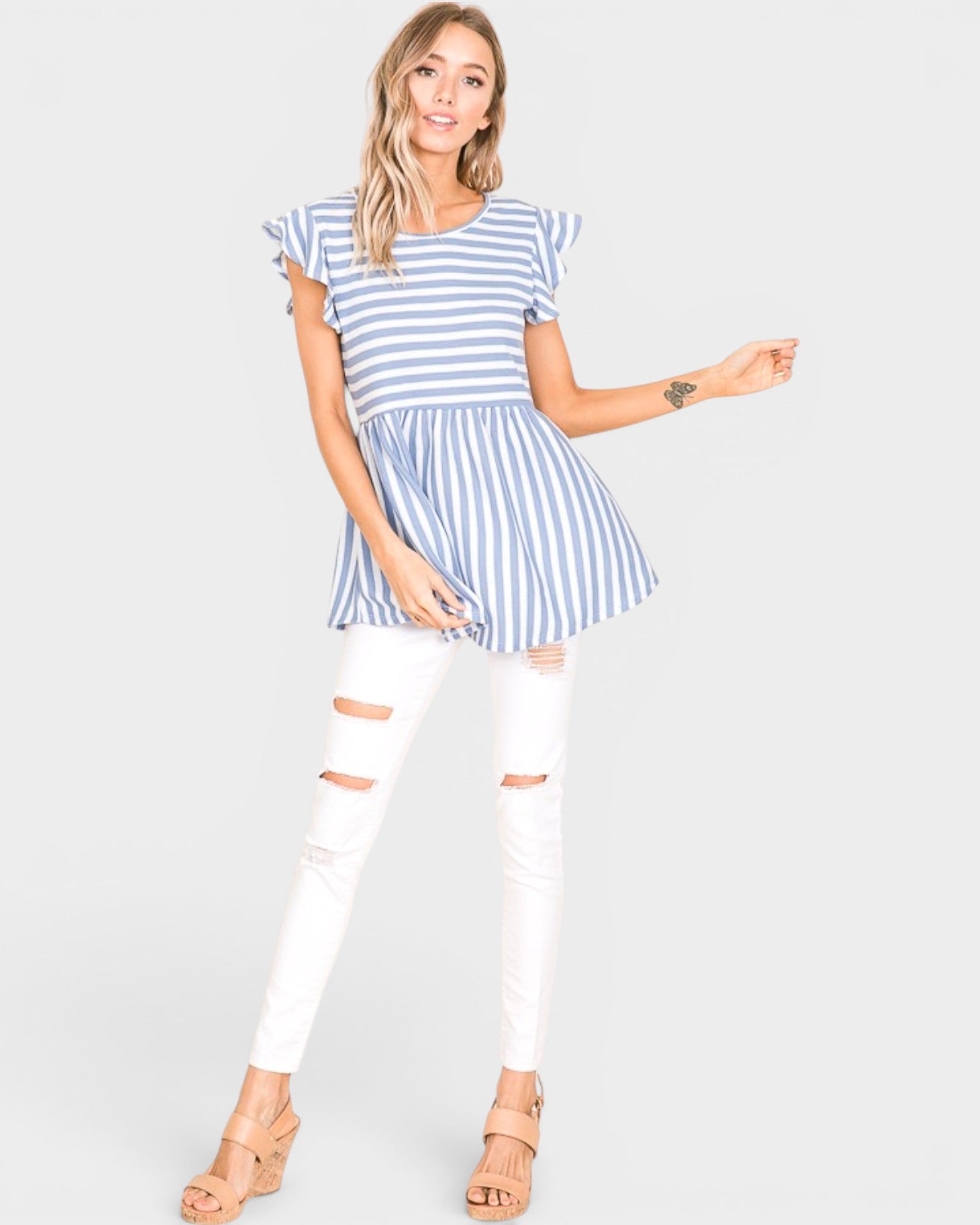Woman wearing a blue and white striped top and white pants on a plain background